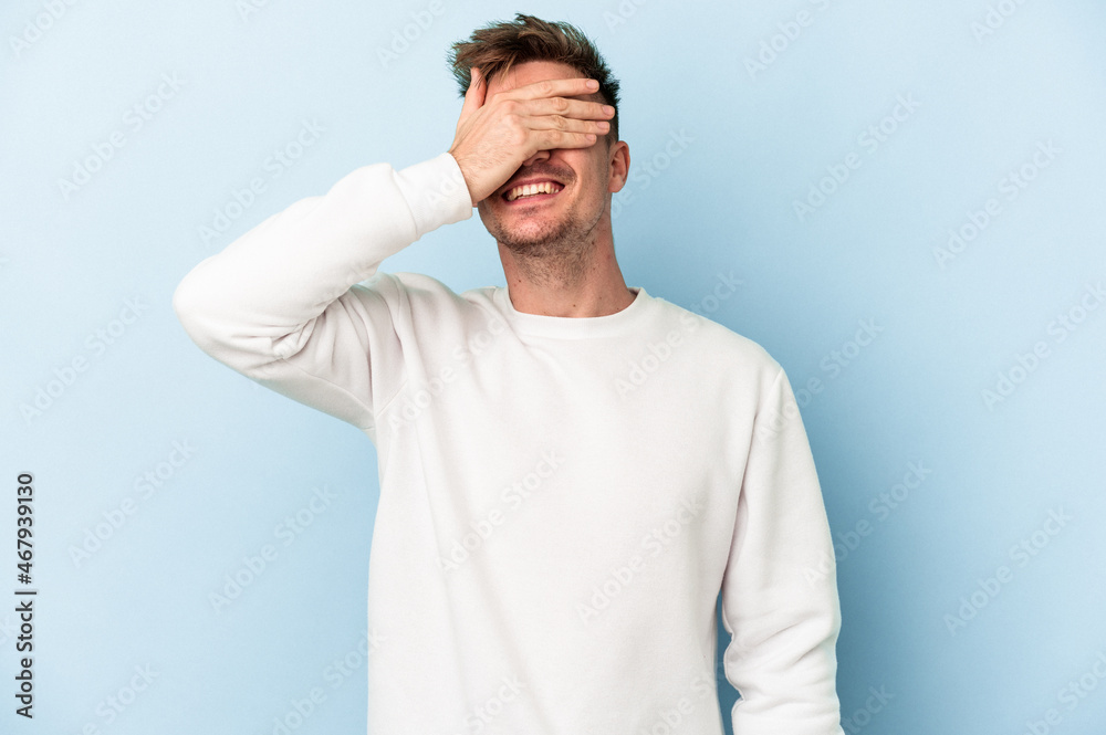 Young caucasian man isolated on blue background covers eyes with hands, smiles broadly waiting for a surprise.