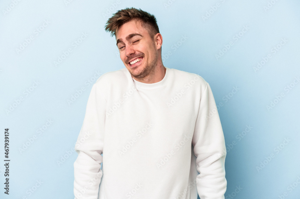 Young caucasian man isolated on blue background laughs and closes eyes, feels relaxed and happy.