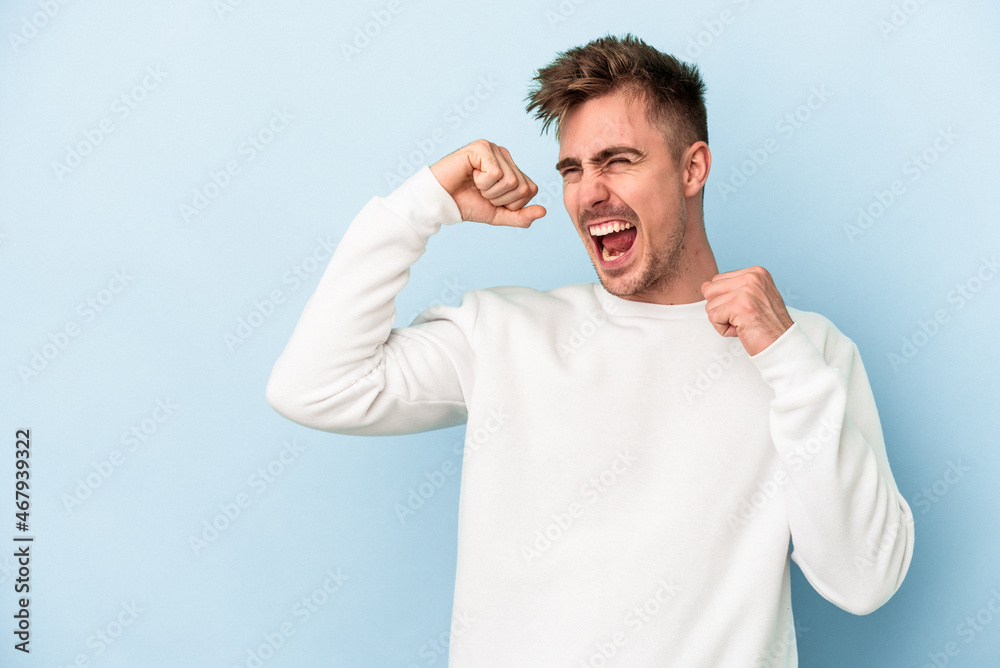 Young caucasian man isolated on blue background raising fist after a victory, winner concept.