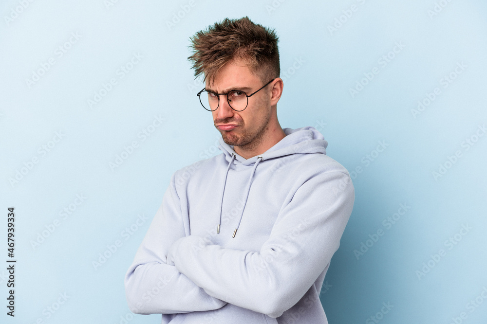Young caucasian man isolated on blue background frowning face in displeasure, keeps arms folded. Young caucasian man isolated on blue background frowning face in displeasure, keeps arms folded.