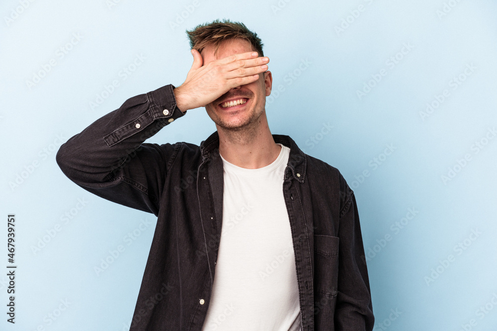 Young caucasian man isolated on blue background covers eyes with hands, smiles broadly waiting for a surprise. Young caucasian man isolated on blue background covers eyes with hands, smiles broadly waiting for a surprise.