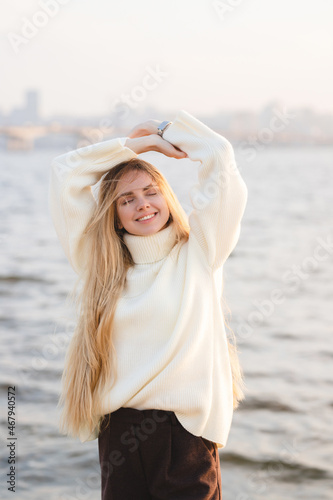 Long-haired blonde girl sitting on the sandy beach in the autumn morning