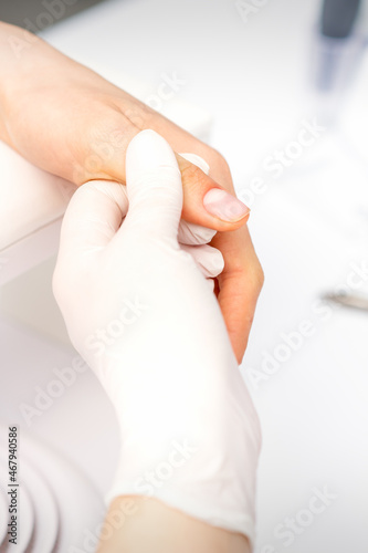 The manicurist holds the female thumb during a manicure procedure in the nail salon