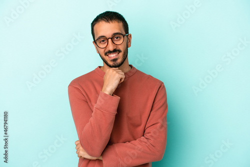 Young caucasian man isolated on blue background smiling happy and confident, touching chin with hand.