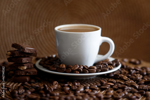 White cup of coffee on the red plate with roasted coffee beans and milk chocolate
