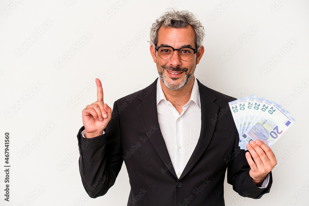 Middle age business man holding bills isolated on blue background  showing number one with finger.