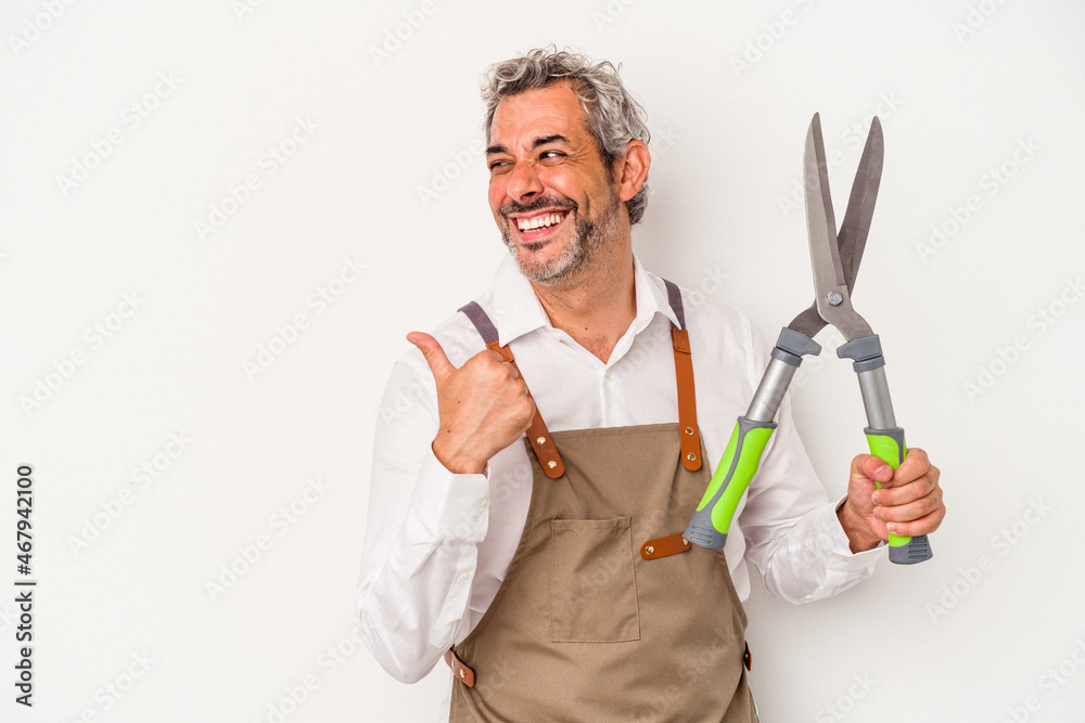 Middle age gardener man holding a scissors isolated on white background points with thumb finger away, laughing and carefree. Middle age gardener man holding a scissors isolated on white background points with thumb finger away, laughing and carefree.