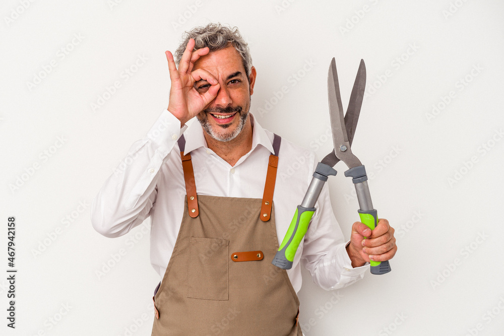 Middle age gardener man holding a scissors isolated on white background excited keeping ok gesture on eye. Middle age gardener man holding a scissors isolated on white background excited keeping ok gesture on eye.