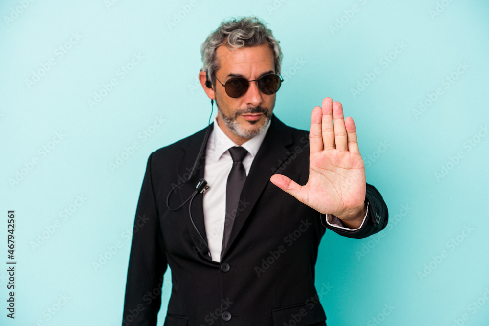 Middle age bodyguard caucasian man isolated on blue background standing with outstretched hand showing stop sign, preventing you. Middle age bodyguard caucasian man isolated on blue background standing with outstretched hand showing stop sign, preventing you.