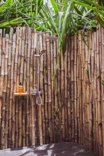 Outdoor shower with bamboo wall and palm tree. Bathroom in tropical hotel. Vacations in Africa. Tropical lifestyle. Shower in garden. Resort faucets concept. Bamboo in hotel design. Asian hotel style.