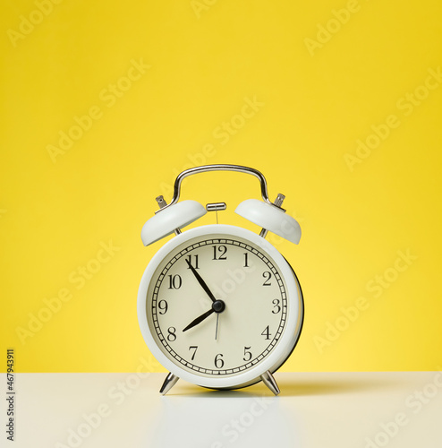 round white alarm clock, five minutes to eight in the morning. Yellow background