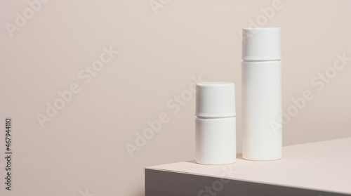 empty white plastic tubes for cosmetics stands on a wooden podium on a beige background. Containers for cream, shampoos, liquid substances. Branding, template