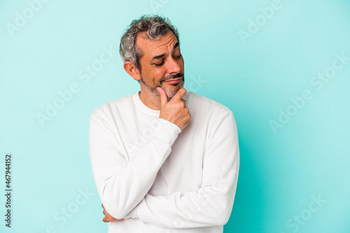 Middle age caucasian man isolated on blue background  looking sideways with doubtful and skeptical expression.