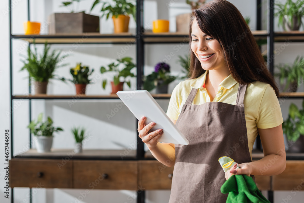 Cheerful florist holding gloves and digital tablet in flower shop Cheerful florist holding gloves and digital tablet in flower shop