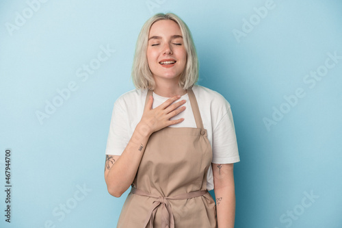 Foto Young caucasian store clerk woman isolated on blue background laughs out loudly keeping hand on chest