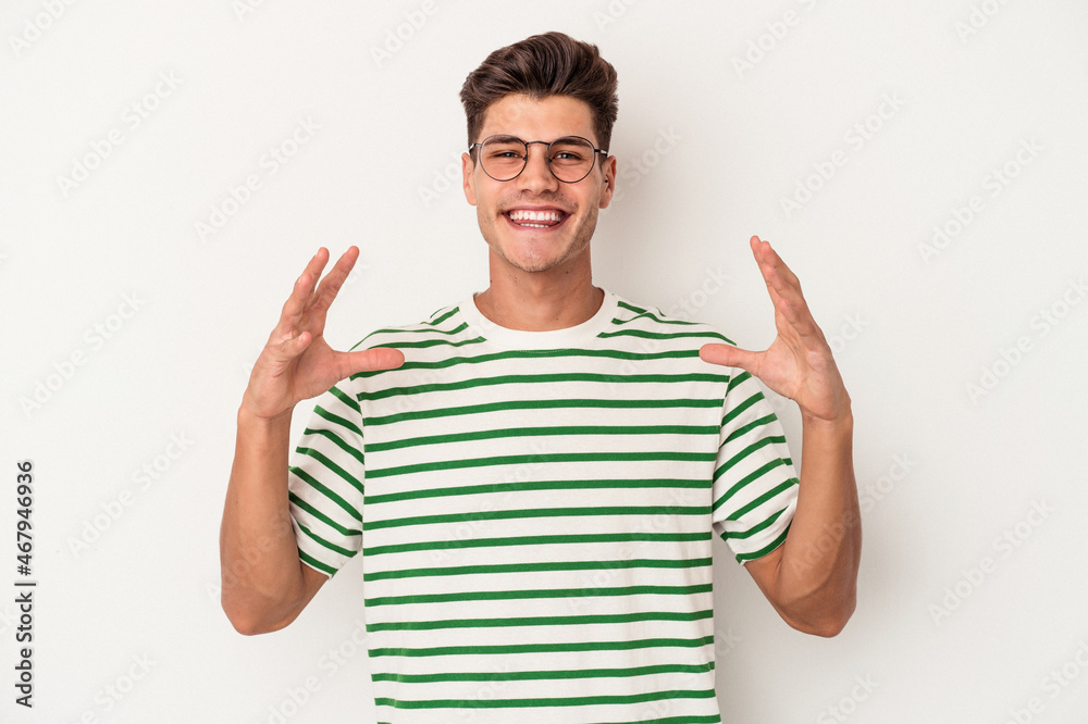 Young caucasian man isolated on white background holding something with palms, offering to camera.