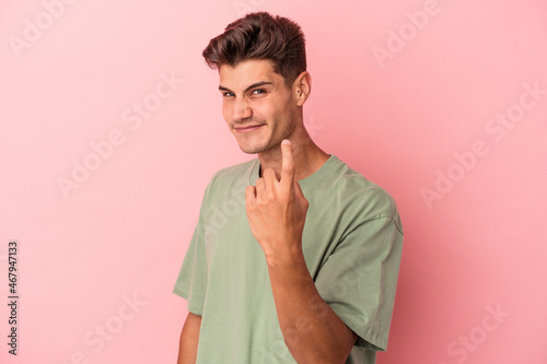 Young caucasian man isolated on pink background pointing with finger at you as if inviting come closer.