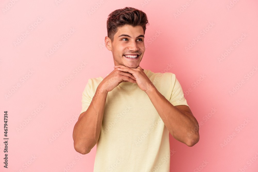Young caucasian man isolated on pink background keeps hands under chin, is looking happily aside. Young caucasian man isolated on pink background keeps hands under chin, is looking happily aside.