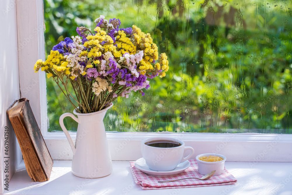 Old book, colorful bouquet of flowers and white cup of tea on background of window with raindrops at home at summer day Old book, colorful bouquet of flowers and white cup of tea on background of window with raindrops at home at summer day