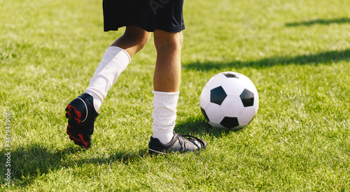 Football Running With Ball on Fresh Grass Field. Boy in Cleats Kicking White and Black Soccer Ball. Soccer Horizontal Background