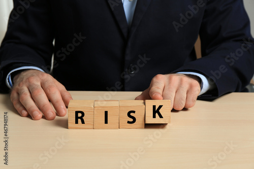 Businessman making word Risk of cubes at wooden table, closeup