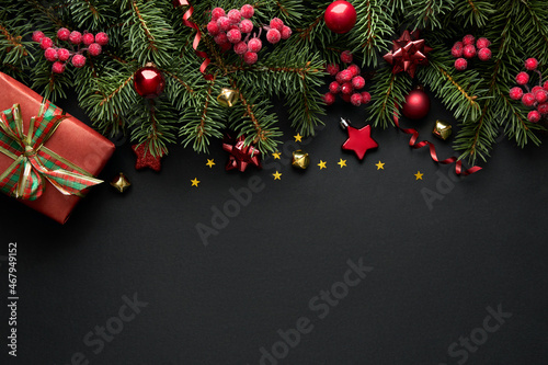 Black Christmas background with Christmas tree branches and red berries  winter festive composition with copy space. Top view.