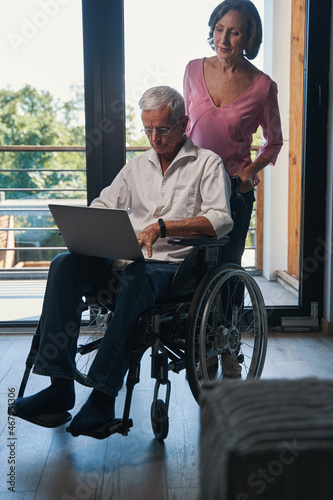 Aged woman pushing wheelchair with her husband working on laptop © Viacheslav Yakobchuk