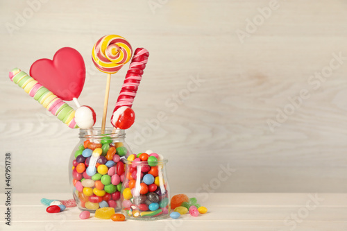 Jars with different delicious candies on beige wooden table, space for text