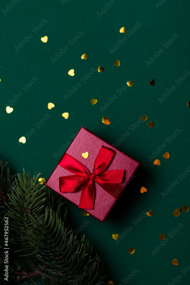 Obraz premium Red gift box with bow and sequins on a green background front view. Christmas gift flat lei