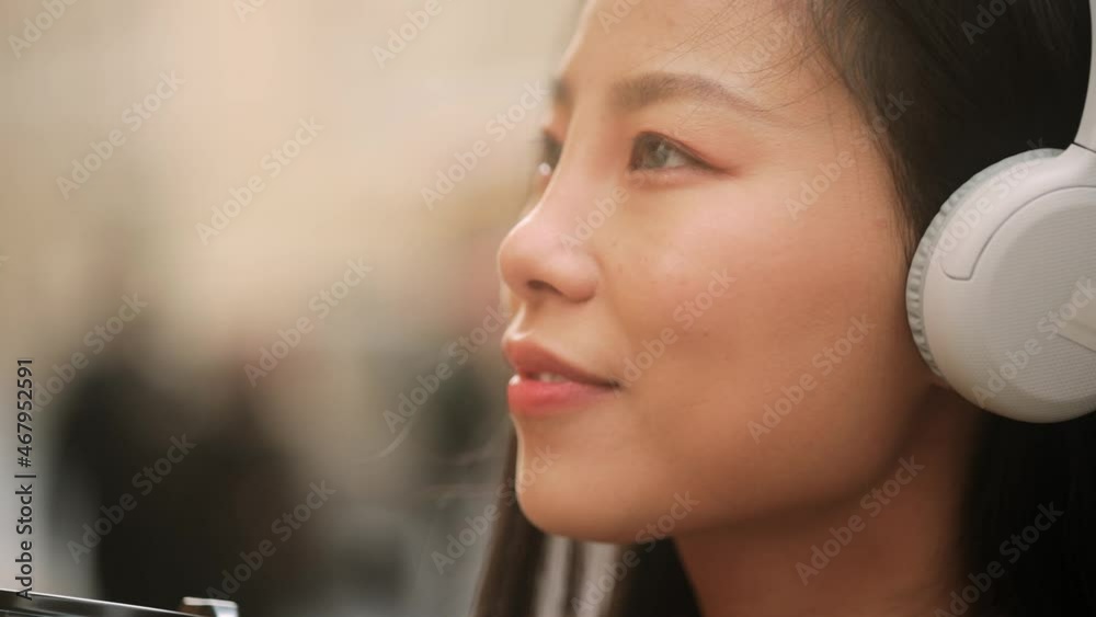 Portrait of young beautiful asian woman in headphones looking ahead at the city street. Close up of happy young girl smiling. High quality 4k footage Portrait of young beautiful asian woman in headphones looking ahead at the city street. Close up of happy young girl smiling. High quality 4k footage