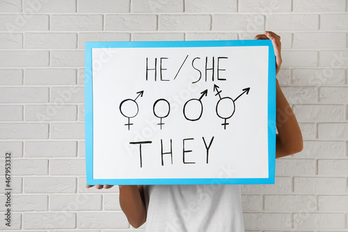 Woman holding sign with gender pronouns and symbols near white brick wall photo