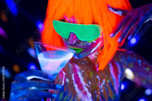 Fashion model woman drinking alcoholic cocktail in neon light, disco night club. Beautiful dancer model girl colorful bright fluorescent make-up