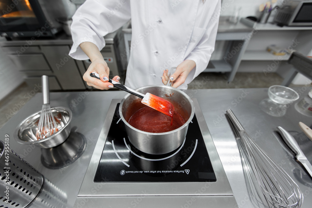 Pastry chef cooks strawberry puree with sugar in a saucepan