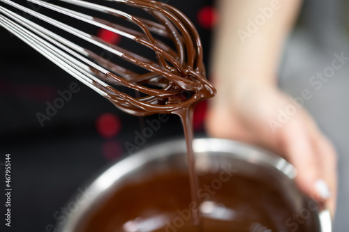 Pastry chef whips melted chocolate in a bowl with a metal wire whisk close up