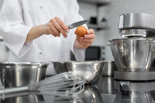 Hands of a pastry chef break an egg with a knife in a professional kitchen