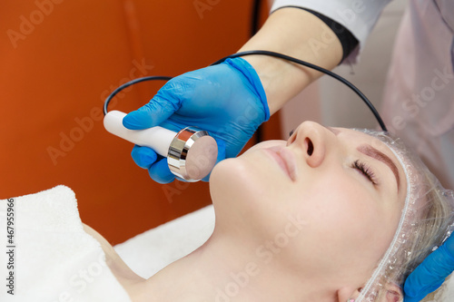 A young woman receives the procedure from a cosmetologist. Hardware korretsky face shape. Cavitation in the cosmetology room.