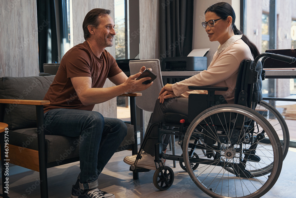 Jolly man with smartphone in office with female with disability Jolly man with smartphone in office with female with disability