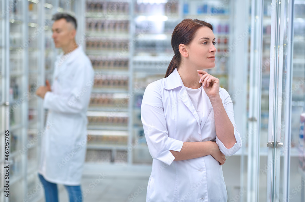 Pensive woman in uniform and employee at pharmacy