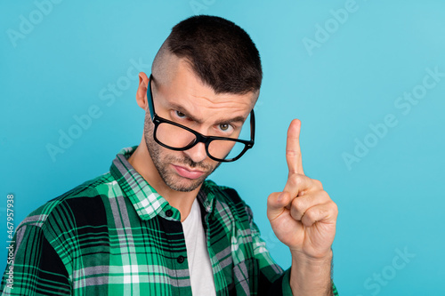 Photo of young unhappy man point finger warning rule bad mood wear glasses isolated on blue color background