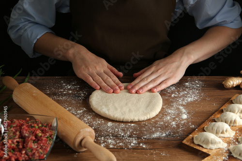 Woman kneading dough for gyoza at wooden table, closeup