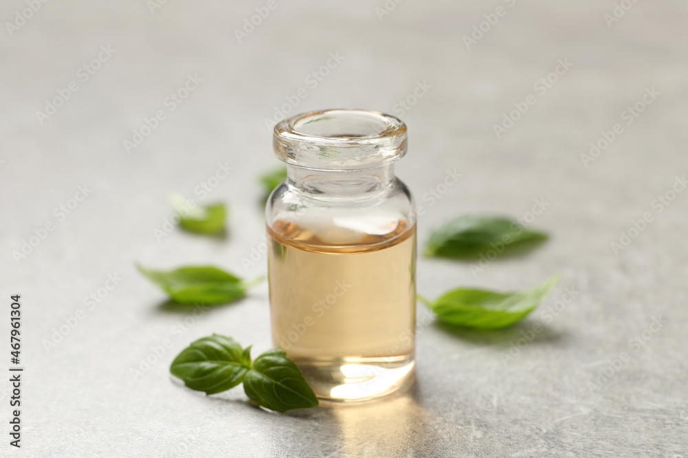 Glass bottle of basil essential oil and leaves on light grey table, closeup Glass bottle of basil essential oil and leaves on light grey table, closeup