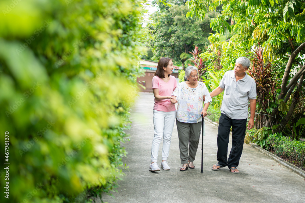 Happy family walking together in the garden. Old elderly using a walking stick to help walk balance. Concept of Love and care of the family And health insurance for family Happy family walking together in the garden. Old elderly using a walking stick to help walk balance. Concept of Love and care of the family And health insurance for family