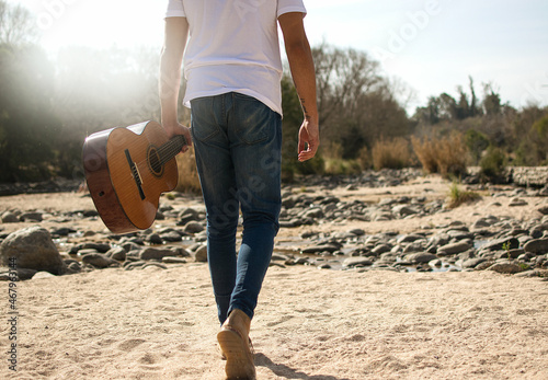 Hombre musico caminando por paisaje con un guitarra en un día soleado