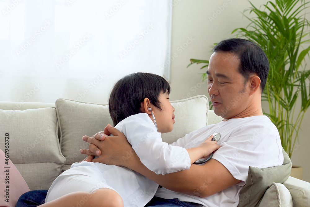 Asian father and son playing doctor and patient The son uses a stethoscope to listen to his father's heartbeat. Asian father and son playing doctor and patient The son uses a stethoscope to listen to his father's heartbeat.