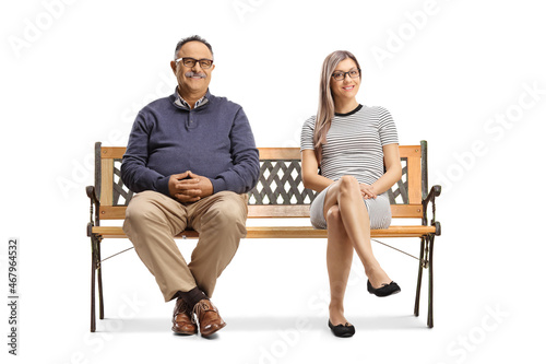 Mature man and a young blond woman sitting on a bench and looking at camera