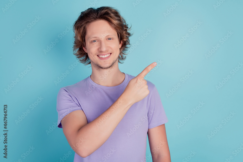 Photo of cheerful young guy point finger empty space advert promotion suggest sale isolated on teal color background Photo of cheerful young guy point finger empty space advert promotion suggest sale isolated on teal color background