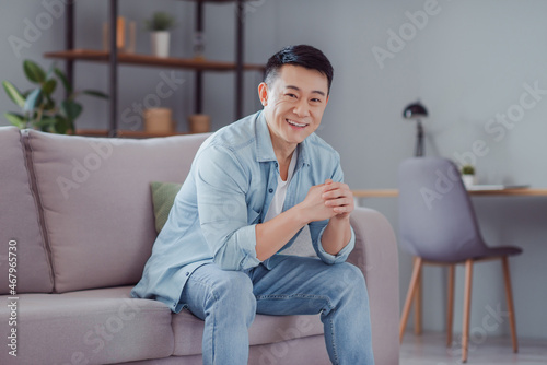 Photo of relaxed cheerful glad japanese man sit couch weekend rest concept wear casual shirt in home indoors