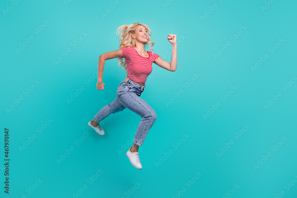 Photo of adorable shiny young lady wear striped t-shirt jumping high running fast looking empty space smiling isolated turquoise color background
