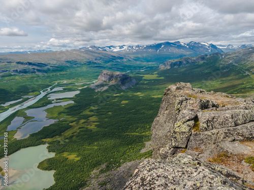 Aerial scenic view from Skierffe rock summit on glacial Rapadalen river delta valley at Sarek national park with meanders, lakes, mountains and birch trees. Summer day landscape Sweden Lapland