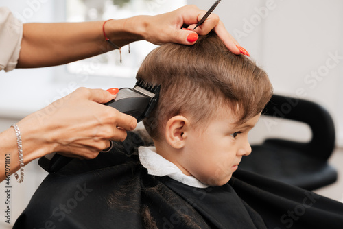 Shooting in a beauty salon. A barber cuts the hair of a little boy with a machine.
